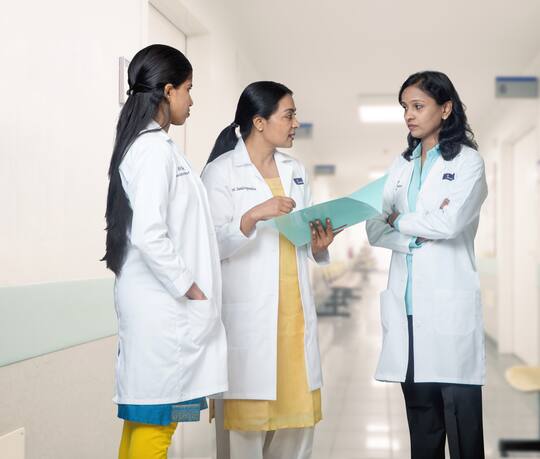 சென்னை நீலாங்கரை ஜனனம் ஃபெர்ட்டிலிட்டி சென்டரின் நடைபாதையில் Dr Vani Sundarapandian‑ம் இரண்டு ஜனனம் சகாக்களும் சேர்ந்து ஒரு வழக்குக் கோப்பைப் படிக்கிறார்கள்