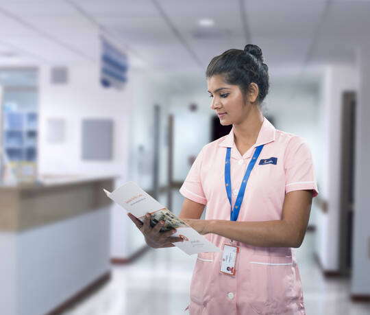 சென்னை நீலாங்கரை மருத்துவமனையின் நடைபாதையில் பணியில் இருக்கும் ஜனனம் செவிலியர், ஒரு நோயாளி கோப்பைப் படிக்கிறார்
